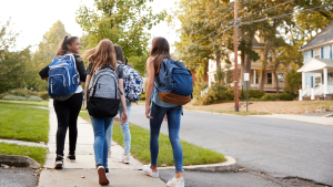 4 middle school girls with backpacks on walking down the sidewalk to school.