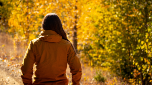 Woman walking outside on a bright sunny day in the fall. Yellow leaves surround her on the trees.